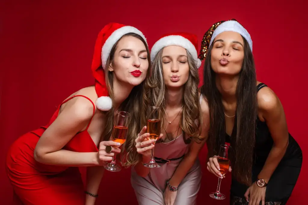 Three women in festive Santa hats celebrating Christmas with champagne, promoting Gaia in Love’s collection of toys for her.