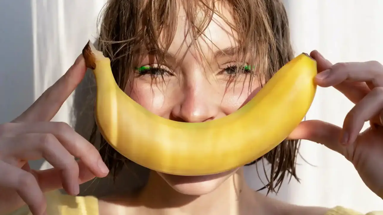 A joyful young woman holding a banana, symbolizing playfulness and empowerment through Gaia in Love's innovative female vibrators.