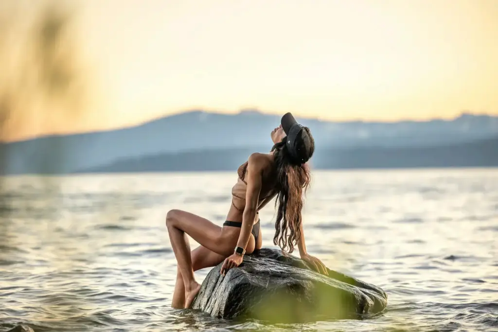 A confident woman posing on a rock near the water at sunset, embodying freedom and empowerment, aligning with Gaia in Love's mission to inspire women worldwide.