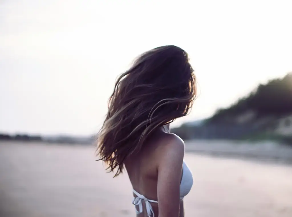 A serene woman with flowing hair standing on the beach, symbolizing natural beauty and individuality—values championed by Gaia in Love.