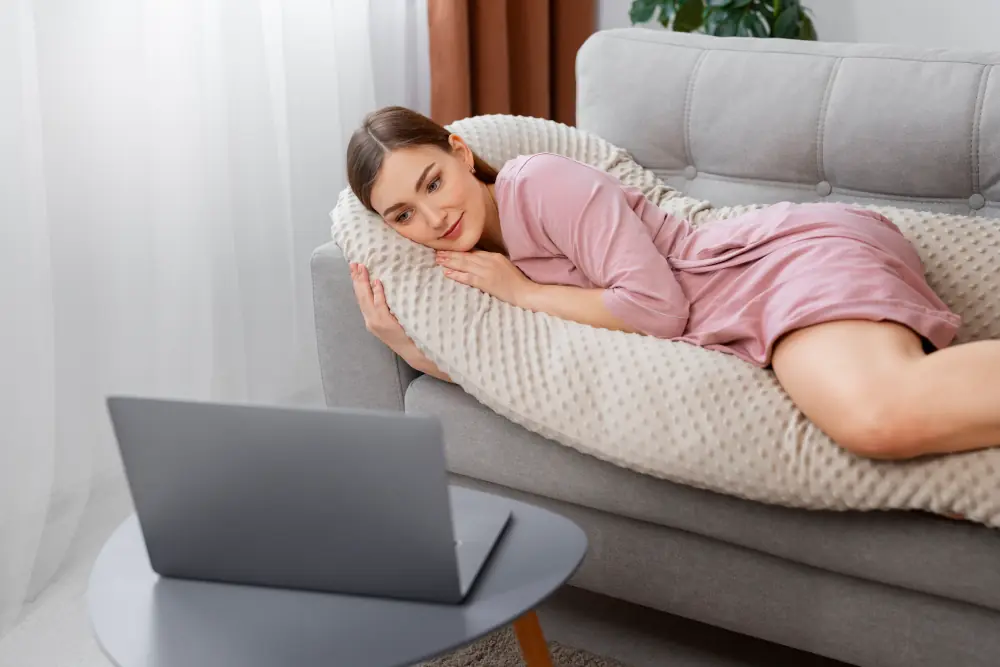 Happy woman lounging on a sofa with a laptop, symbolizing self-care and relaxation. Enhance your moments with Gaia in Love’s rabbit bibrator.