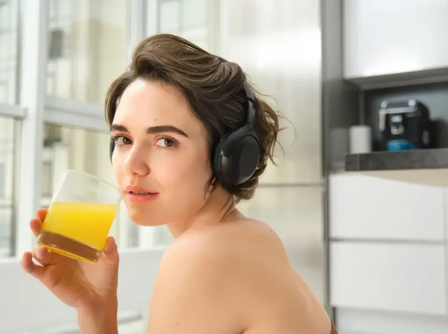 Sporty woman enjoying juice with headphones, reflecting health and lifestyle, incorporating magic wands wellness tools by Gaia in Love.