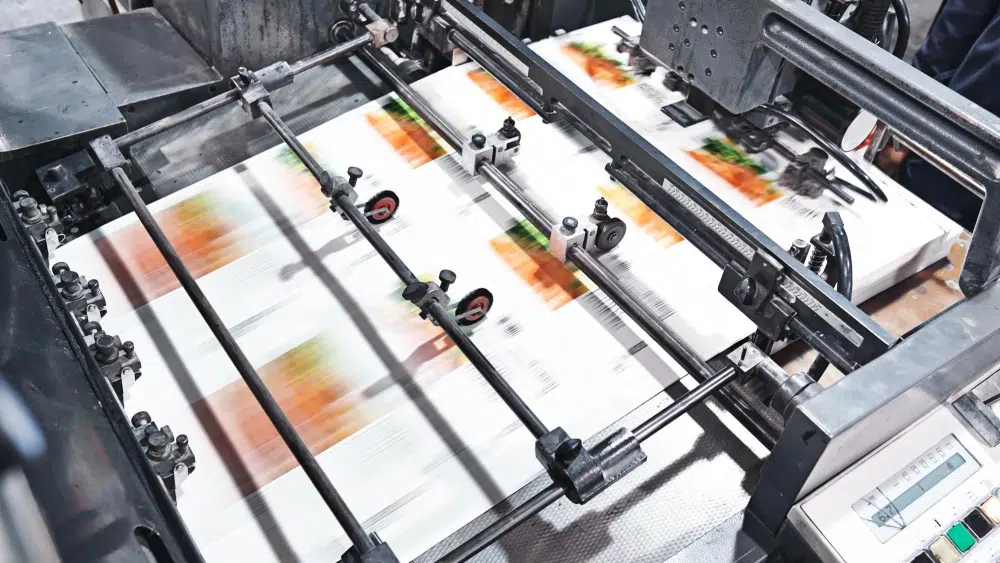 Offset printing press running full-color packaging sheets for custom retail box production.