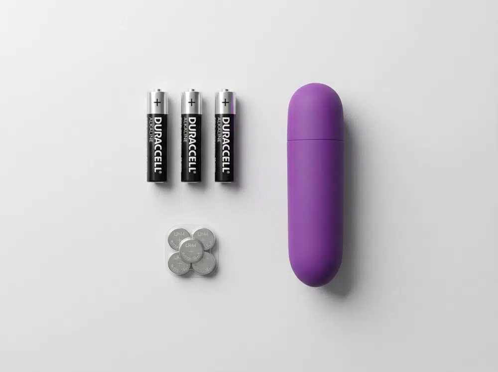 Purple bullet vibrator with replaceable batteries (AAA and button cells) on a light gray background.
